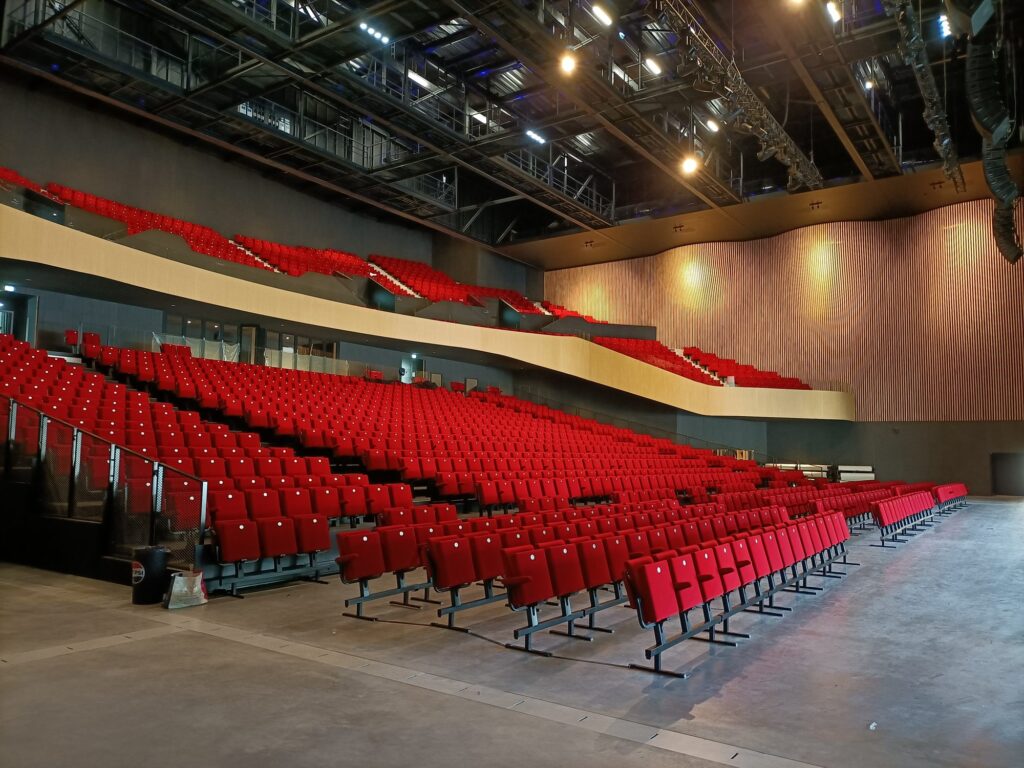 Grande salle de spectacle aux fauteuils rouges, balcon et mur de bois