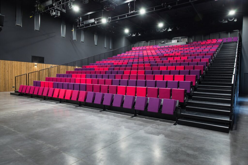 Tribunes télescopiques à fauteuils rouges et violets dans une salle de spectacle (La Prade, Pradines) – Hugon Tribunes